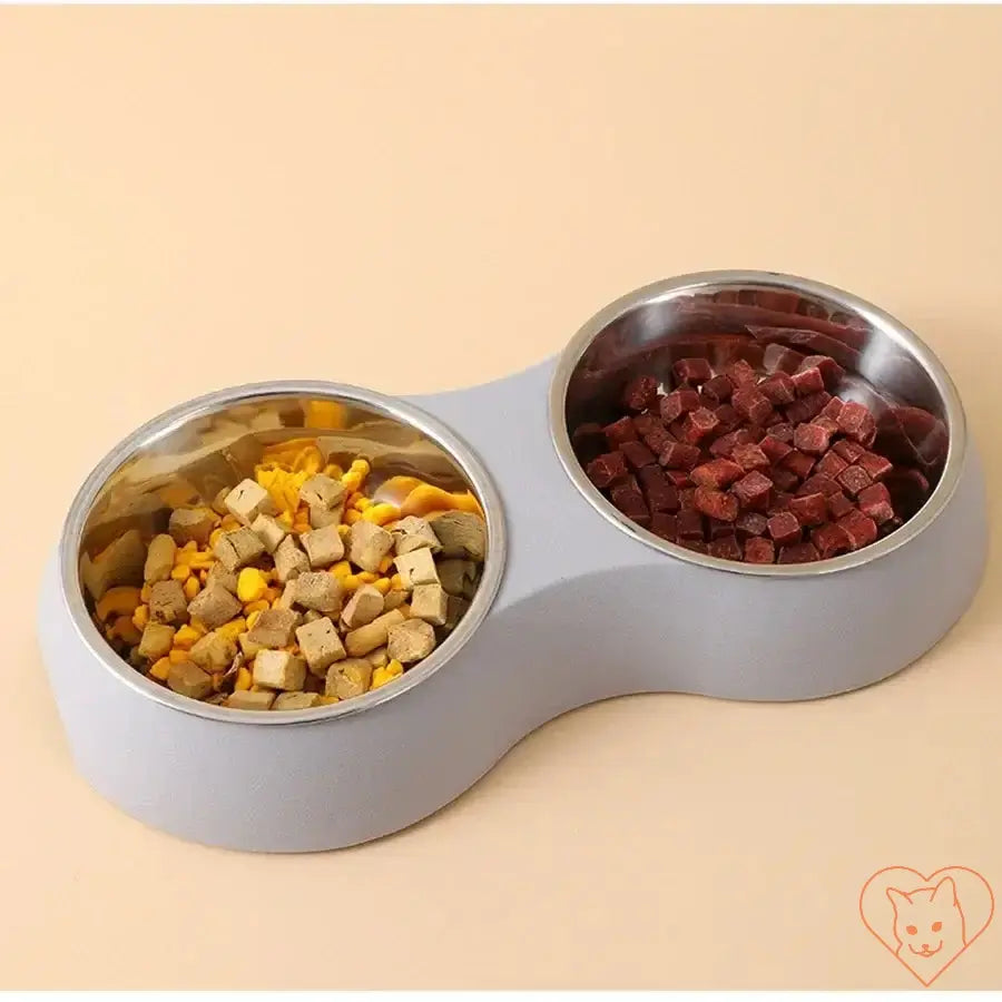 Double stainless steel pet food bowl set with dry dog food and treats in a sleek gray base.