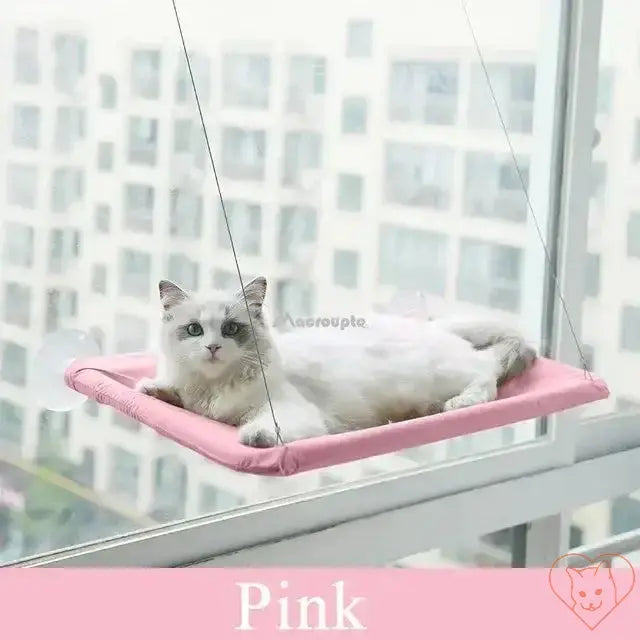 Cat relaxing in a pink hanging hammock by a window, enjoying the view in comfort.