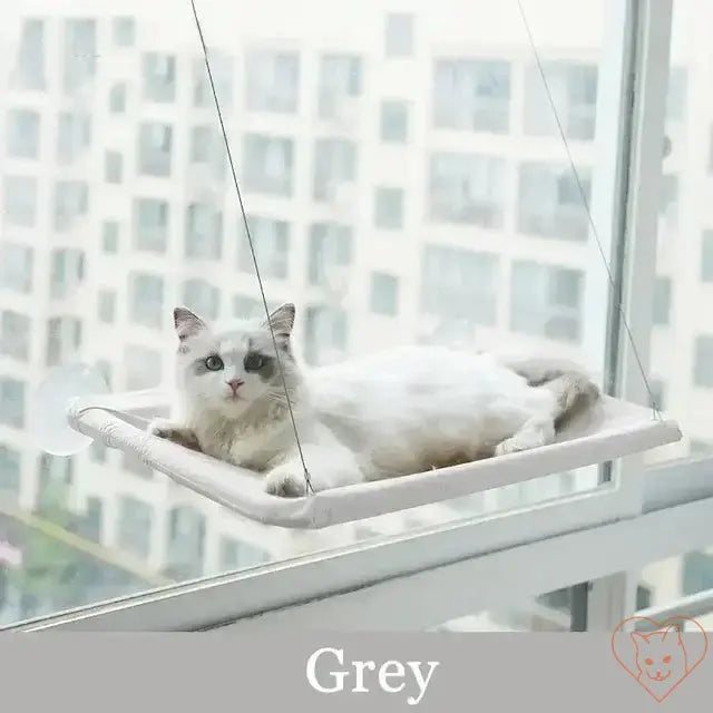 Grey hanging cat hammock featuring a white cat lounging in a sunny window, providing a cozy spot for relaxation.