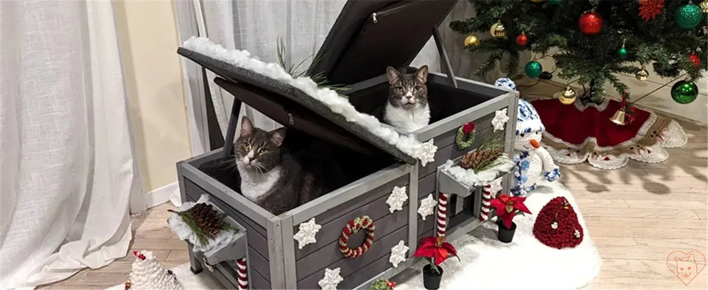 Two cats inside a festive insulated outdoor cat house decorated for winter holidays.