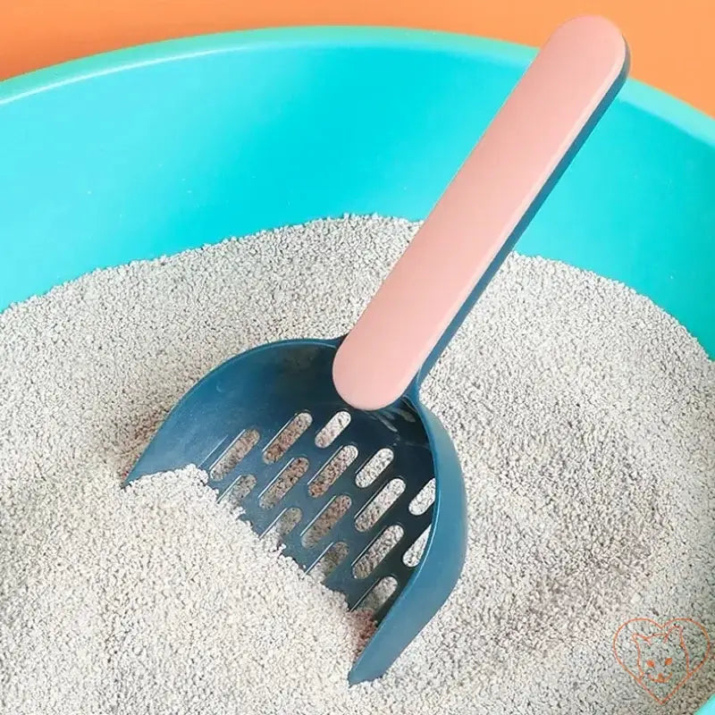 Plastic cat litter scoop resting in a blue litter box, designed for efficient cleaning and easy use.