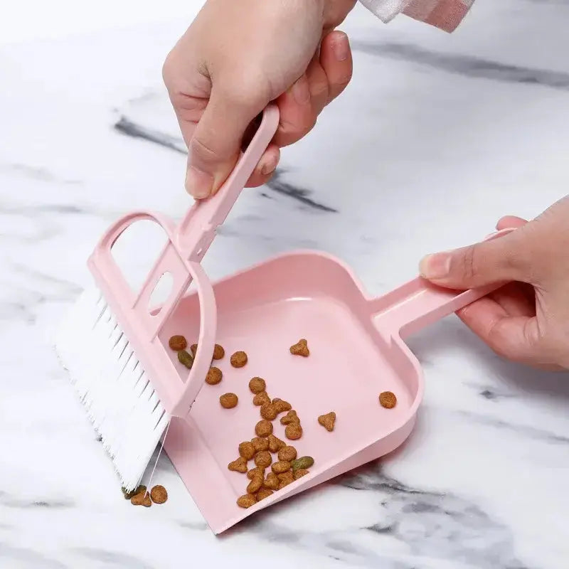 Person using a small pink broom and dustpan set to clean up pet food from a marble surface.