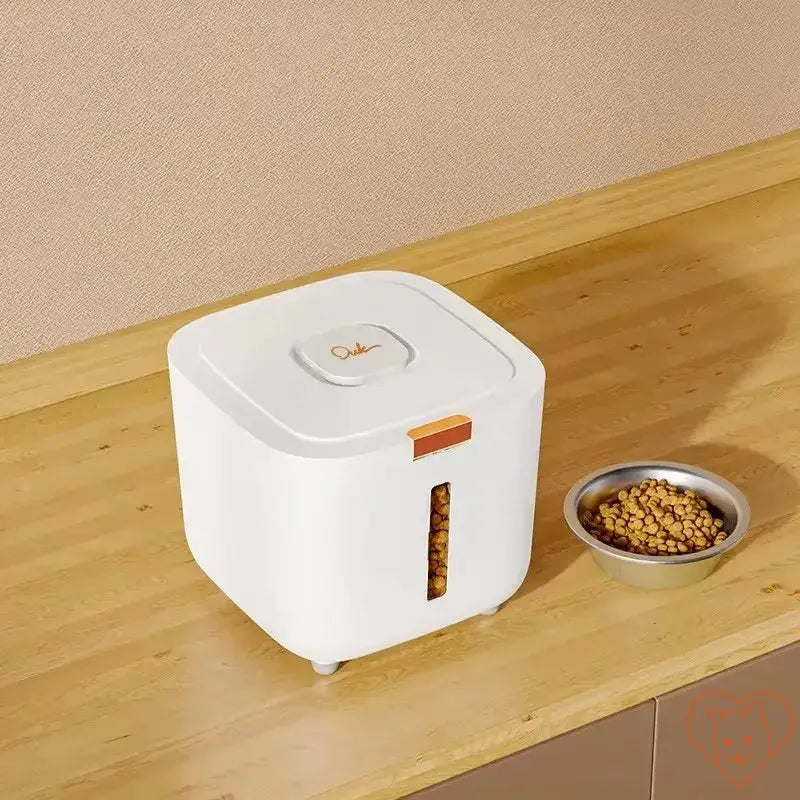 Sealed cat food storage barrel in white with orange accents, next to a bowl of cat food on a wooden countertop.