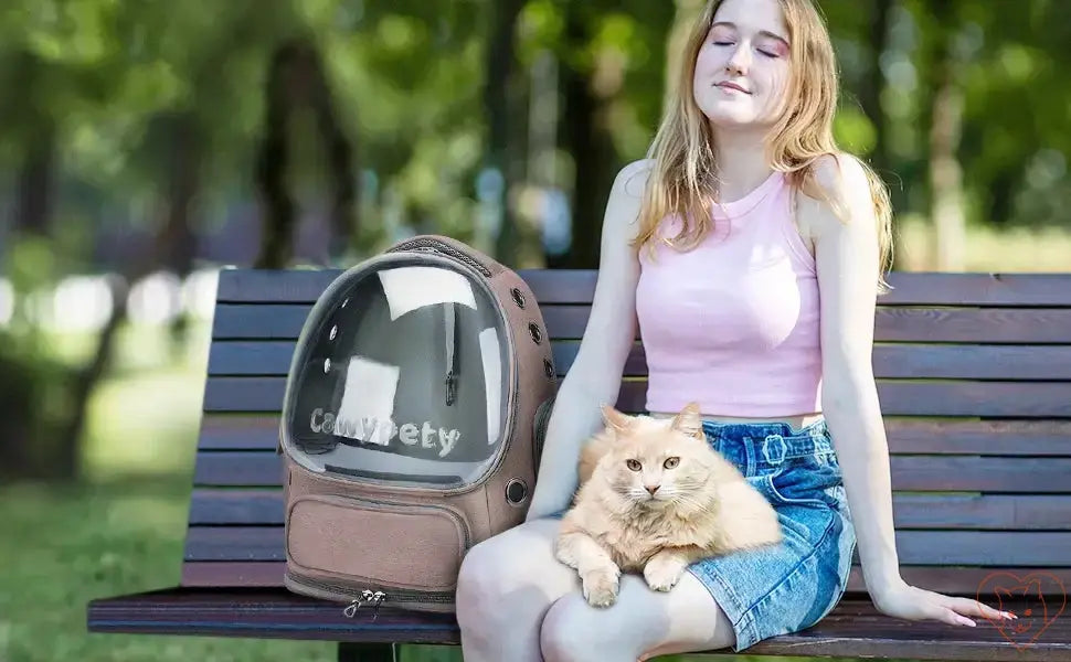 Woman sitting on a bench with a transparent pet carrier backpack and a fluffy orange cat.