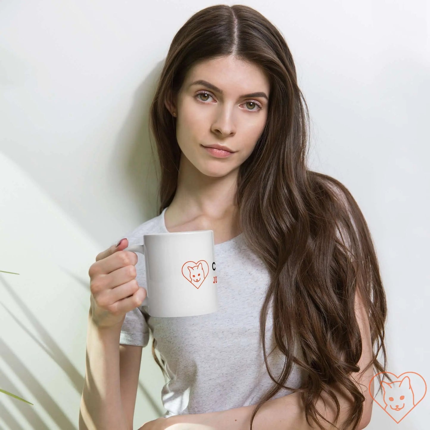 Woman holding a white glossy mug with a cat logo, wearing a gray t-shirt, showcasing a stylish drink experience.